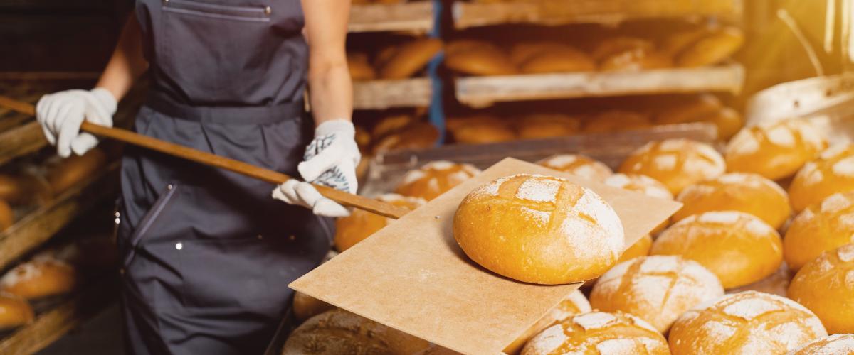 pék kenyeret tart sütőlapáton